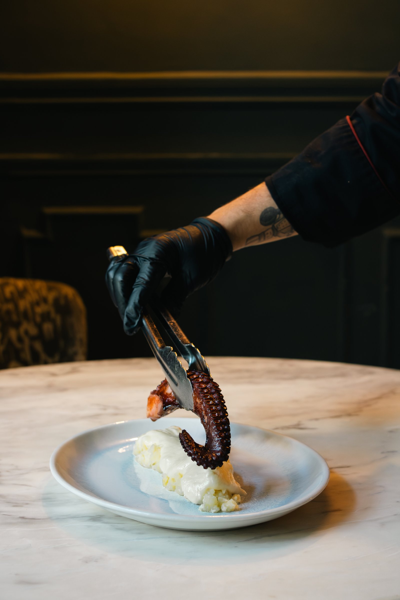 Chef con guante negro emplatando pulpo sobre fondo negro